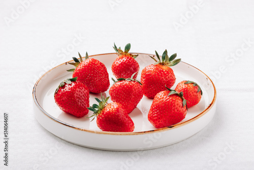 A few ripe juicy strawberries in a plate on a white background