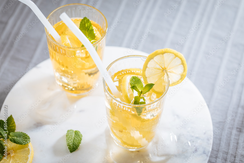 Ice tea with lemon and mint leaves. Served with ice on marble background. Summer refreshing cocktail drink
