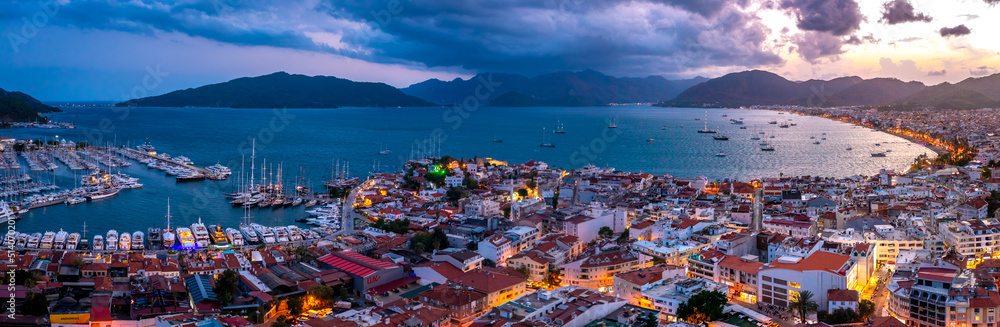 Aerial view of Marmaris harbor with yacht and sailboat with evening lighting. Colorful landscape of the night Turkish city. Beautiful sky at sunset