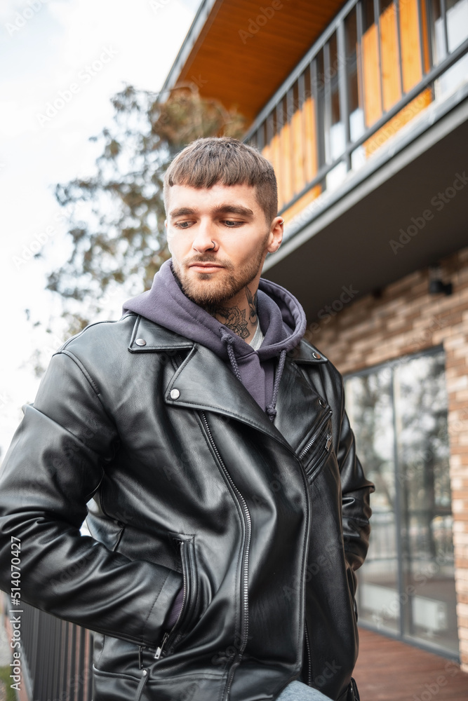 Street fashion handsome hipster man with hair and beard in a fashionable black leather jacket and hoodie on the street Street fashion handsome hipster man with hair and beard in a fashionable black leather jacket and hoodie on the street