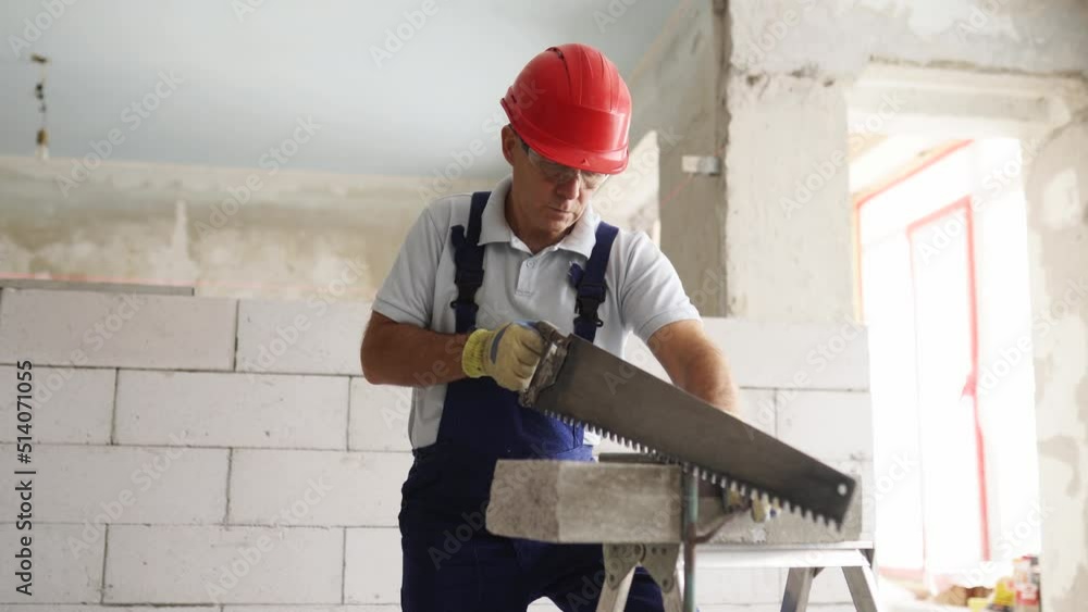 Bricklayer worker sawing foam concrete block with hand saw. Contractor cuts autoclaved aerated concrete blocks on construction site. Concept of building your own home. Bricklayer worker sawing foam concrete block with hand saw. Contractor cuts autoclaved aerated concrete blocks on construction site. Concept of building your own home.