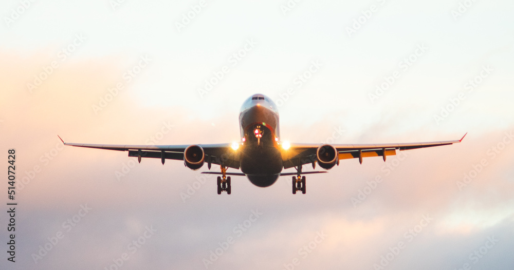 The silhouette of a passenger plane coming in for landing against the backdrop of the sunset sky.