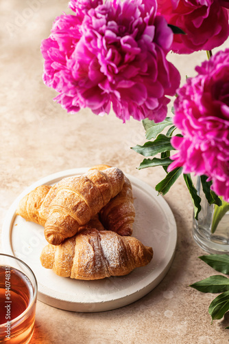 Plate of fresh croissants  tea and peonies flowers for breakfast on brown background with text space