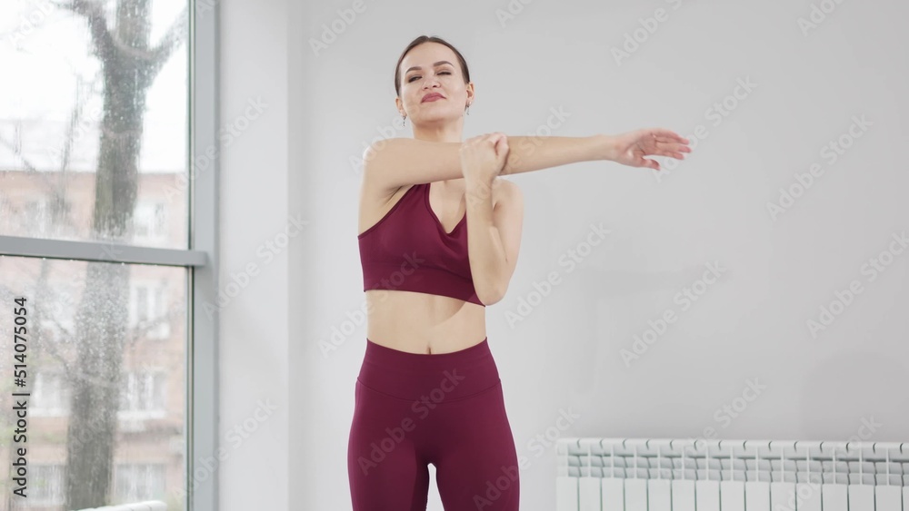 a woman in a burgundy tracksuit exercises in a gym. warm-up and stretching.