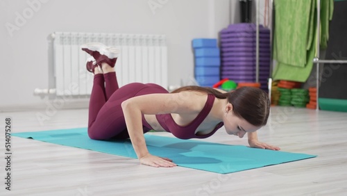 a beautiful and slender woman in a burgundy tracksuit exercises on a mat