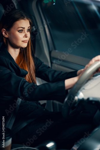vertical photo of a pleasant, relaxed woman sitting behind the wheel of a car with a seat belt fastened, smiling pleasantly. Photography at night © SHOTPRIME STUDIO