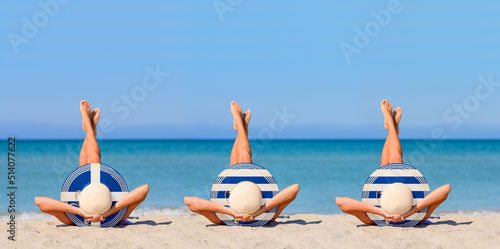 Three young girls on the beach wearing straw hats in the colors of the flag of Greece. The concept of the perfect holiday in the resorts of the Greece. Focus on hats.
