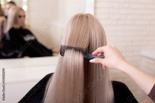 
Hairdresser's hand brushing long silver blonde hair in beauty salon
