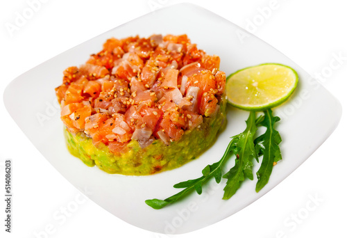 Salmon tartare with guacamole served on white circular plate with slice of lime and arugula. Isolated over white background