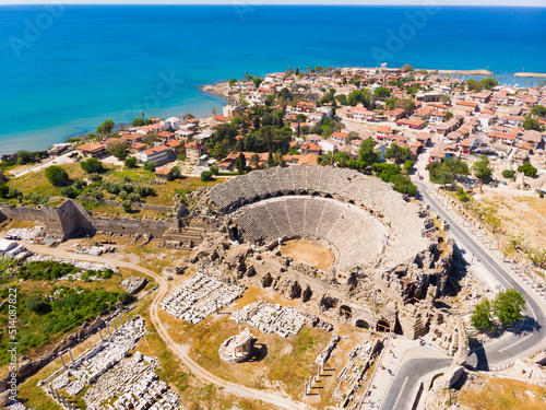 Drone view of ancient ruined Roman theater on background of Side cityscape on coast of blue Mediterranean Sea on sunny spring day. Archaeological and historical sights of modern Turkey
