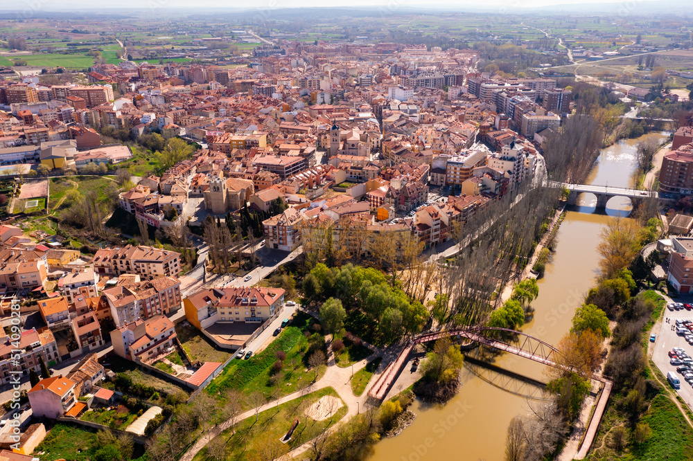 Scenic drone view of modern residential areas of Aranda de Duero city on banks of Duero river on sunny spring day on background of natural rural landscape, Burgos, Spain