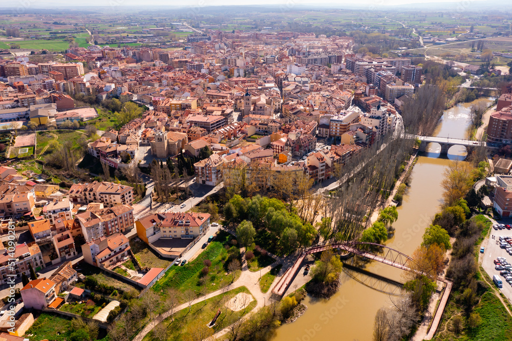 Fototapeta premium Scenic drone view of modern residential areas of Aranda de Duero city on banks of Duero river on sunny spring day on background of natural rural landscape, Burgos, Spain