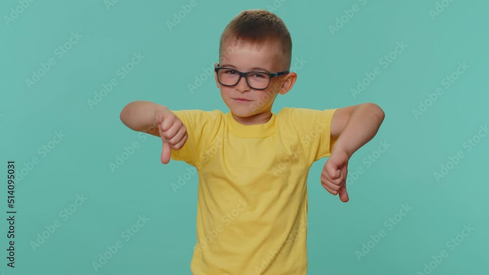 Dislike. Upset little toddler children boy showing thumbs down sign gesture, expressing discontent, disapproval, dissatisfied. Young preschool kid in glasses isolated alone on blue studio background Dislike. Upset little toddler children boy showing thumbs down sign gesture, expressing discontent, disapproval, dissatisfied. Young preschool kid in glasses isolated alone on blue studio background