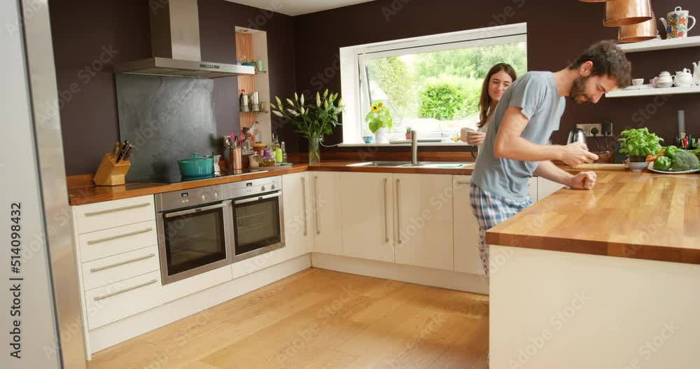 A cheerful young couple dancing in the kitchen to music playing on their smartphone A cheerful young couple dancing in the kitchen to music playing on their smartphone