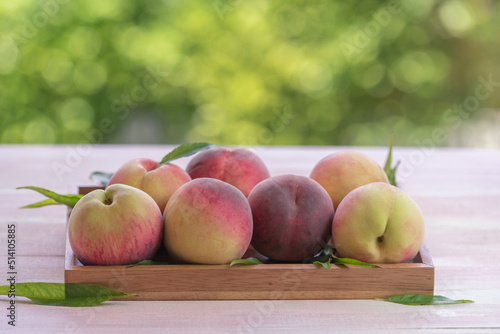 Fresh Sweet Peach on green bokeh background, Pink and yellow Peach fruit with leaf on wooden plate.