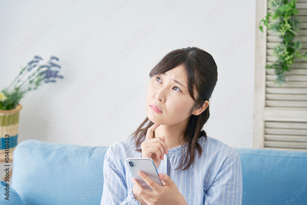 リビングでスマホを使いながら悩む女性