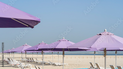 Fototapeta Naklejka Na Ścianę i Meble -  Purple beach umbrellas. Blue sky. Relaxing context. Summer holidays at the sea. General contest and location