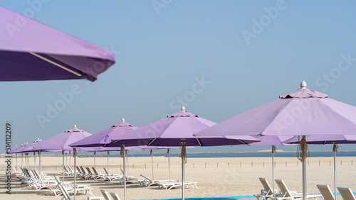 Fototapeta Naklejka Na Ścianę i Meble -  Purple beach umbrellas. Blue sky. Relaxing context. Summer holidays at the sea. General contest and location