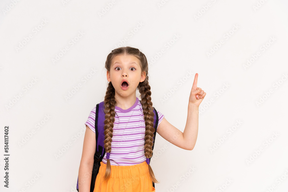 A child with a school backpack points up at your advertisement on a white isolated background. A little girl with pigtails points to the announcement of courses for children. A child with a school backpack points up at your advertisement on a white isolated background. A little girl with pigtails points to the announcement of courses for children.