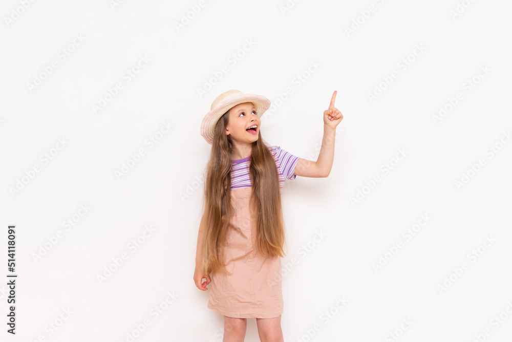 A beautiful little girl in a summer sundress and a straw hat on a white isolated background points her index finger up at your advertisement. A beautiful little girl in a summer sundress and a straw hat on a white isolated background points her index finger up at your advertisement.
