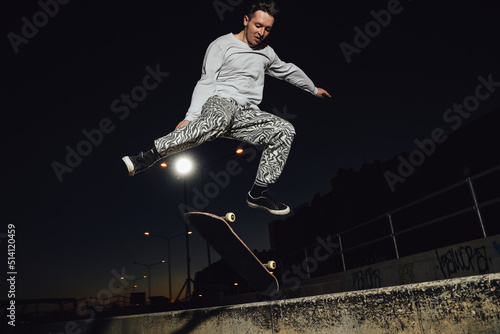 Portrait of professional skateboarder dressed in white casual clothes jumping skateboard.