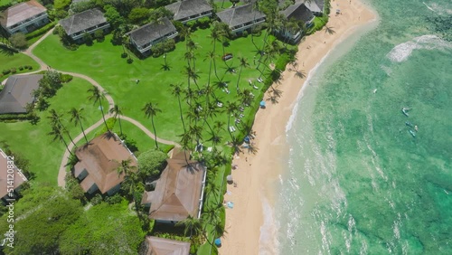 Aerial 4K view of Poipu, Kauai island showing luxury resort and clear blue turquoise beach. People surfing, swimming and tanning on sandy beach. Background of wonderful Pacific beach on Hawaii USA photo