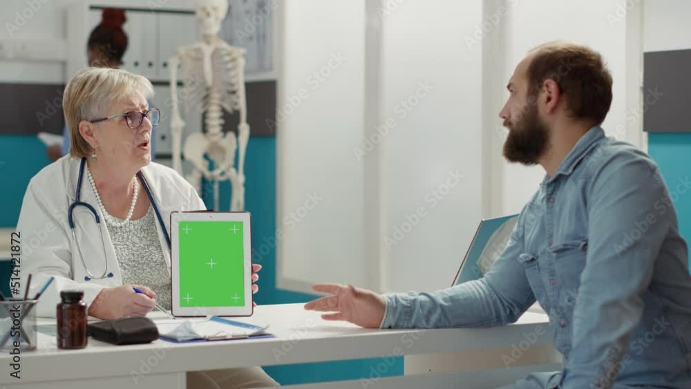Doctor vertically holding greenscreen on digital tablet in cabinet. People at checkup visit looking at mockup template with isolated chromakey background and blank copyspace on display. Doctor vertically holding greenscreen on digital tablet in cabinet. People at checkup visit looking at mockup template with isolated chromakey background and blank copyspace on display.