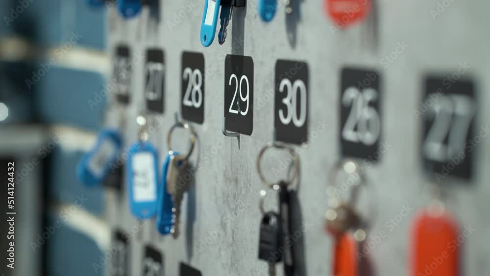 Keys with numbered badges hanging on wall, female hand taking one of them with number twenty nine. Partial view hotel concierge at work giving room key to guest. Concept of hospitality business Keys with numbered badges hanging on wall, female hand taking one of them with number twenty nine. Partial view hotel concierge at work giving room key to guest. Concept of hospitality business