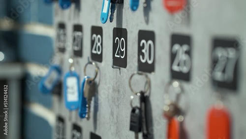 Keys with numbered badges hanging on wall, female hand taking one of them with number twenty nine. Partial view hotel concierge at work giving room key to guest. Concept of hospitality business photo