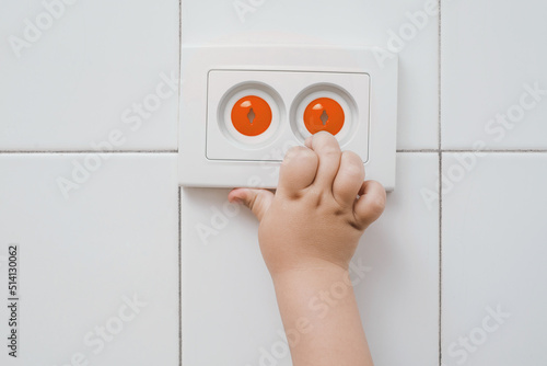 A small child's hand touches an electrical outlet with child safety plugs. The child inserts his finger into the socket. Child safety at home and parental control