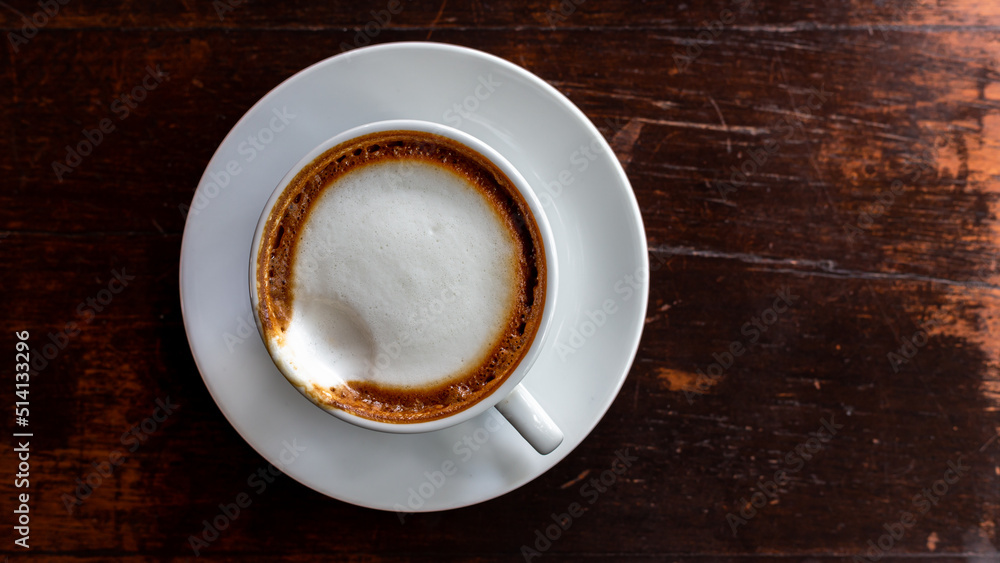 Top view closeup hot cappuccino coffee or latte coffee in white ceramic mug with frothy foam on wooden table background, Top view with copy space, Flat lay coffee cup on wooden. Top view closeup hot cappuccino coffee or latte coffee in white ceramic mug with frothy foam on wooden table background, Top view with copy space, Flat lay coffee cup on wooden.