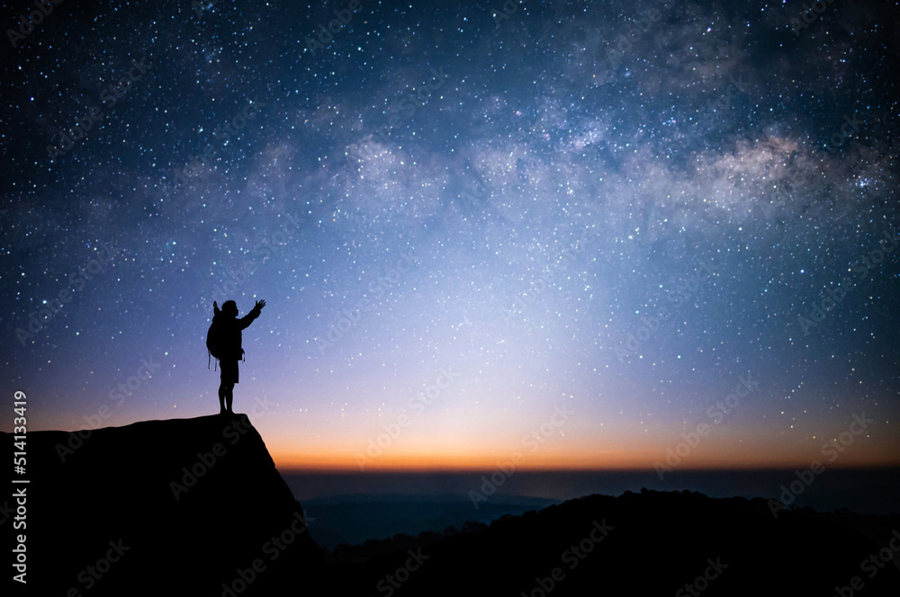 Silhouette of young man standing and watched the star, milky way and night sky alone on top of the mountain. He enjoyed traveling and was successful when he reached the summit.