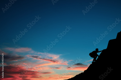 A young tourist with backpack is climbing a cliff alone at sunrise. He had an effort to climb all the way to the top of the mountain and he had to succeed.