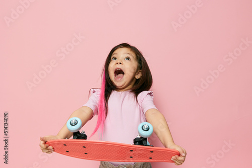 a cute little girl of preschool age is standing on pink in a pink T-shirt, cheerfully shouting and joyfully stretching her skate in front, throwing her head back a little