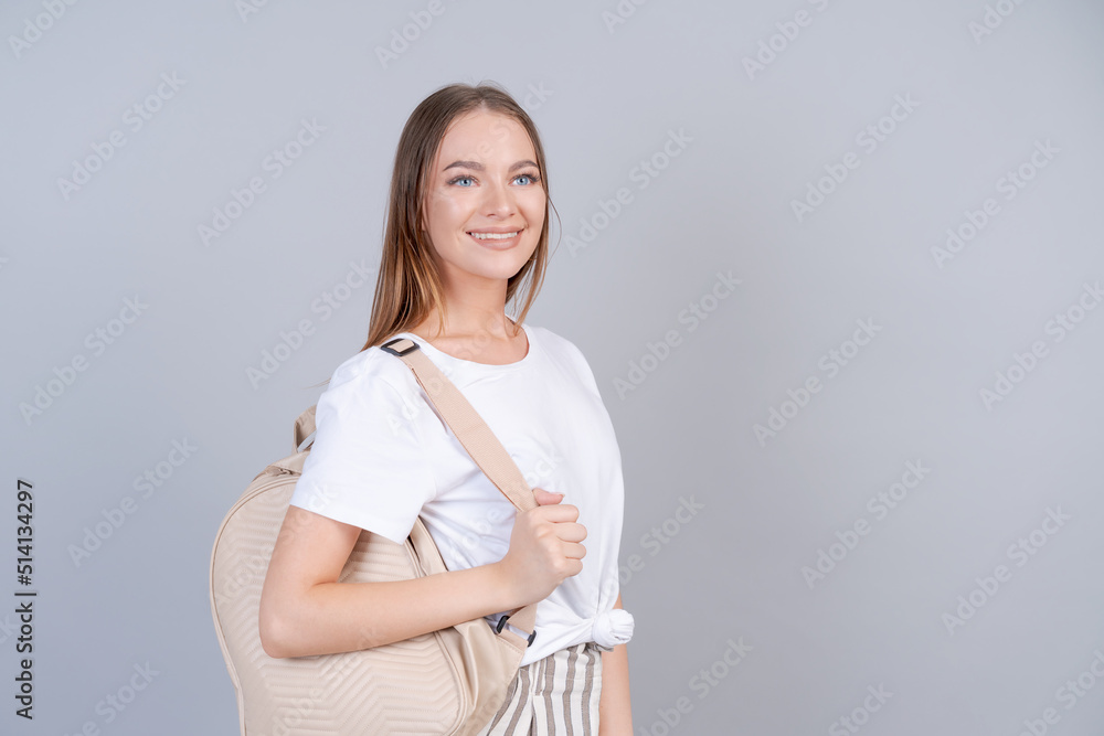Happy female student in light casual clothes stands smiling on gray background in the studio. A young woman with a backpack in a white t-shirt and pants poses fun, advertises and mockup Happy female student in light casual clothes stands smiling on gray background in the studio. A young woman with a backpack in a white t-shirt and pants poses fun, advertises and mockup