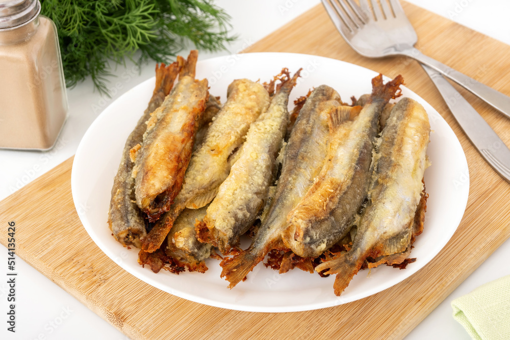 Baked capelin with crispy crust on cutting board. Small fat fish for cheap and healthy diet. Baked capelin with crispy crust on cutting board. Small fat fish for cheap and healthy diet.