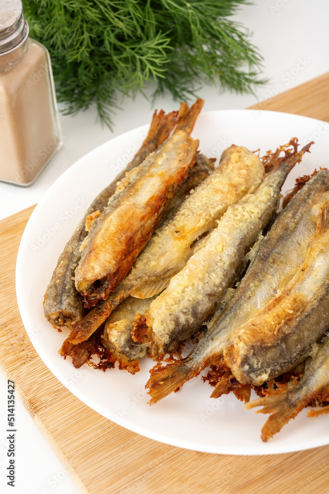 Small fried fish without head on wooden board. Roasted seafood with dill and pepper. Traditional home cuisine dish. Small fried fish without head on wooden board. Roasted seafood with dill and pepper. Traditional home cuisine dish.