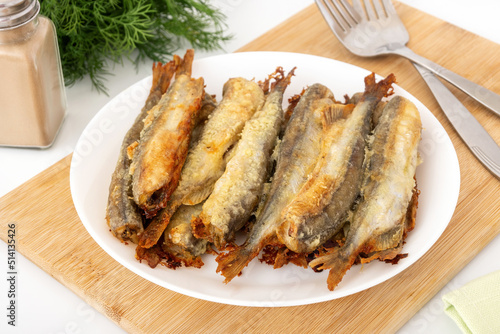 Baked capelin with crispy crust on cutting board. Small fat fish for cheap and healthy diet. photo