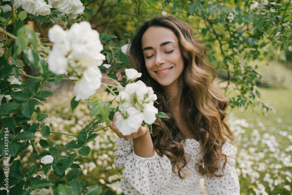 Young beautiful woman with long curly hair wearing white dress relaxing in blooming rose garden. Young beautiful woman with long curly hair wearing white dress relaxing in blooming rose garden.