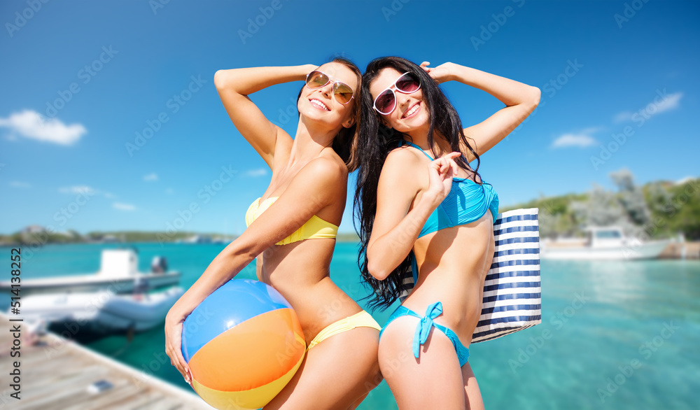 travel, tourism and summer vacation concept - beautiful happy women in bikinis with inflatable ball and bag posing over wooden pier and boat on tropical beach background in french polynesia