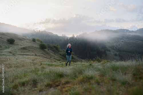 Senior woman jogging in nature on early morning with fog and mountains in background.