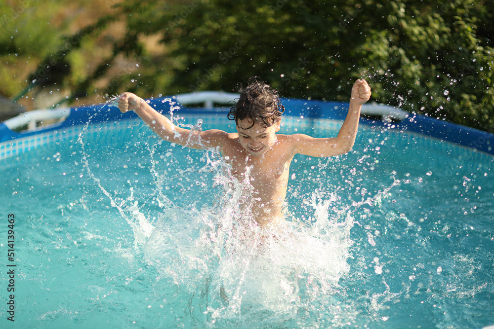 a boy happily splashes in the pool in the summer heat