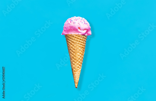 food, dessert and eating concept - close up of pink ice cream in waffle cone with sprinkles over blue background