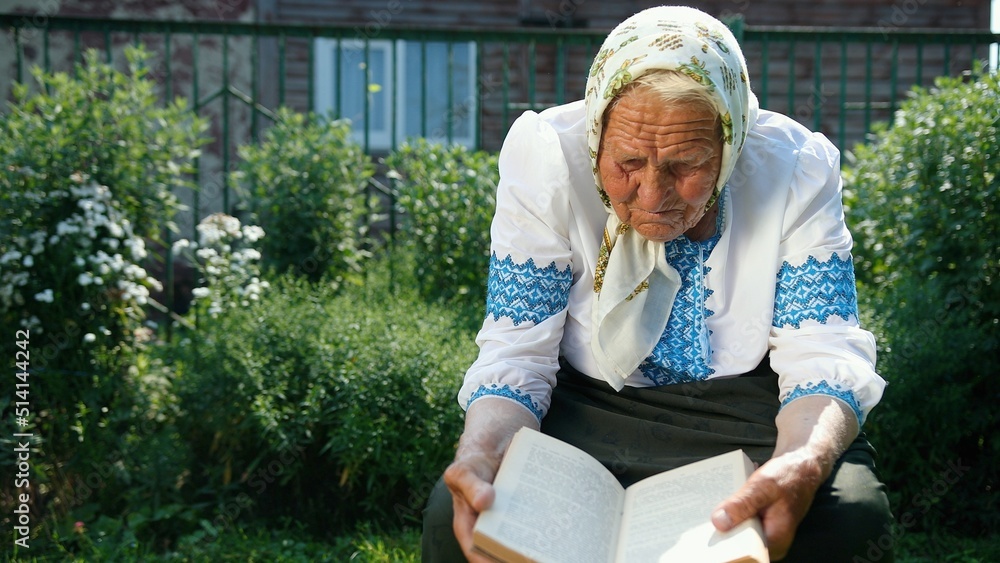 Samolepka An old grandmother is sitting on the street and reading a book
