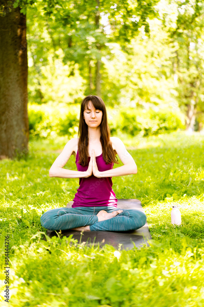A beautiful young woman is sitting on a yoga mat in the park and doing yoga or meditation. Copy space. The concept of active recreation, mental tranquility, fitness and a healthy lifestyle. A beautiful young woman is sitting on a yoga mat in the park and doing yoga or meditation. Copy space. The concept of active recreation, mental tranquility, fitness and a healthy lifestyle.