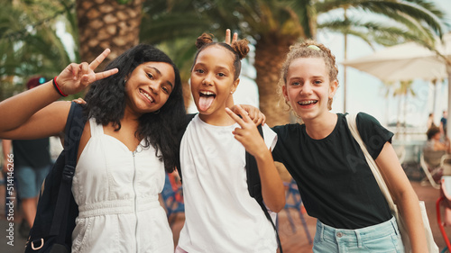 Three girls friends pre-teenage standing on the street smiling, hugging each other making faces for the camera. Three teenagers on the outdoors in urban cityscape background photo