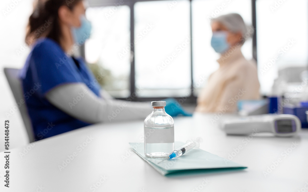 Obraz premium medicine, health and vaccination concept - bottle of medicine and syringe on table over doctor or nurse and patient at hospital