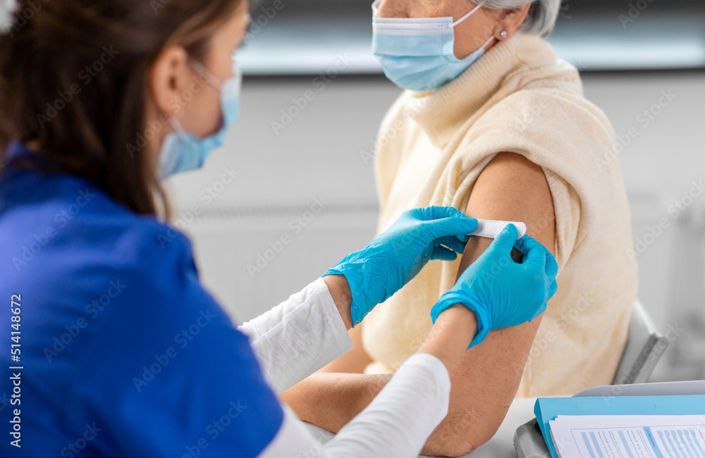 medicine, health and vaccination concept - close up of doctor or nurse applying medical patch to vaccinated senior woman in mask at hospital medicine, health and vaccination concept - close up of doctor or nurse applying medical patch to vaccinated senior woman in mask at hospital