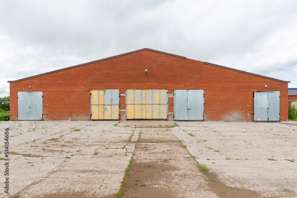 Old closed and abandoned red brick cattle farm building. Rural landscape with cowshed.