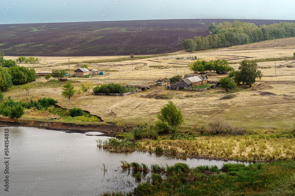 Rural landscape with a village on the banks of a pond and fields. Russia, Orenburg region, farm Arapovka